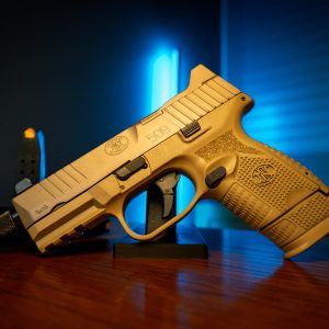 FN 509 Tactical FDE pistol on wood table, blue backlight