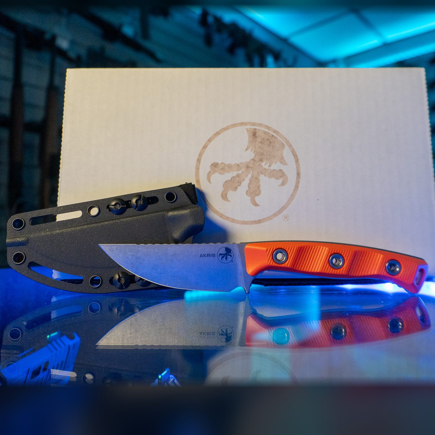 Microtech Akris fixed blade knife with stonewash drop point blade and Ember orange G-10 handle, shown with its black Kydex sheath and Microtech box