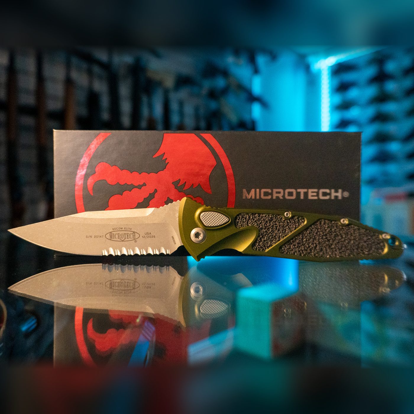 Microtech Socom Elite Auto knife with Apocalyptic finish partially serrated blade and OD green handle with black textured inlays, in front of its Microtech box
