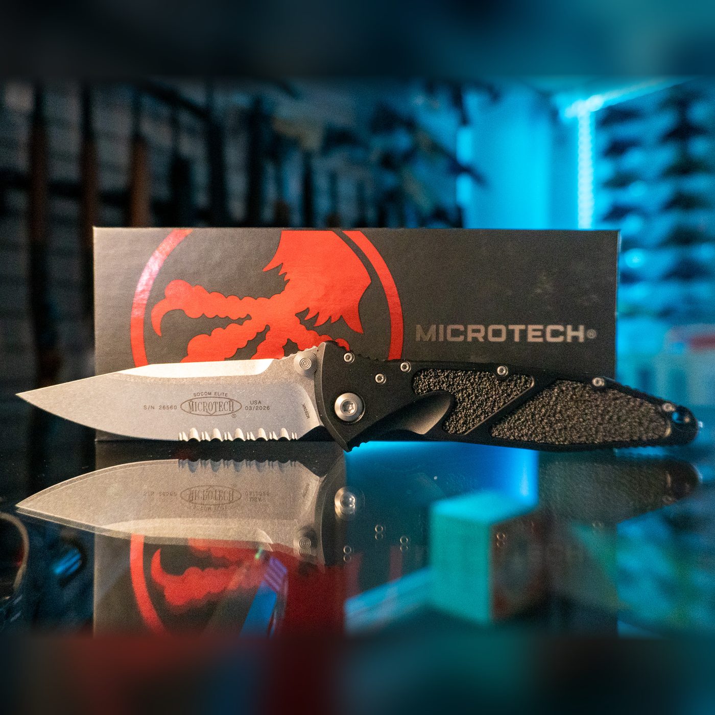 Microtech Socom Elite manual folding knife with stonewash partially serrated blade and black handle with textured grip inlays, in front of its Microtech box