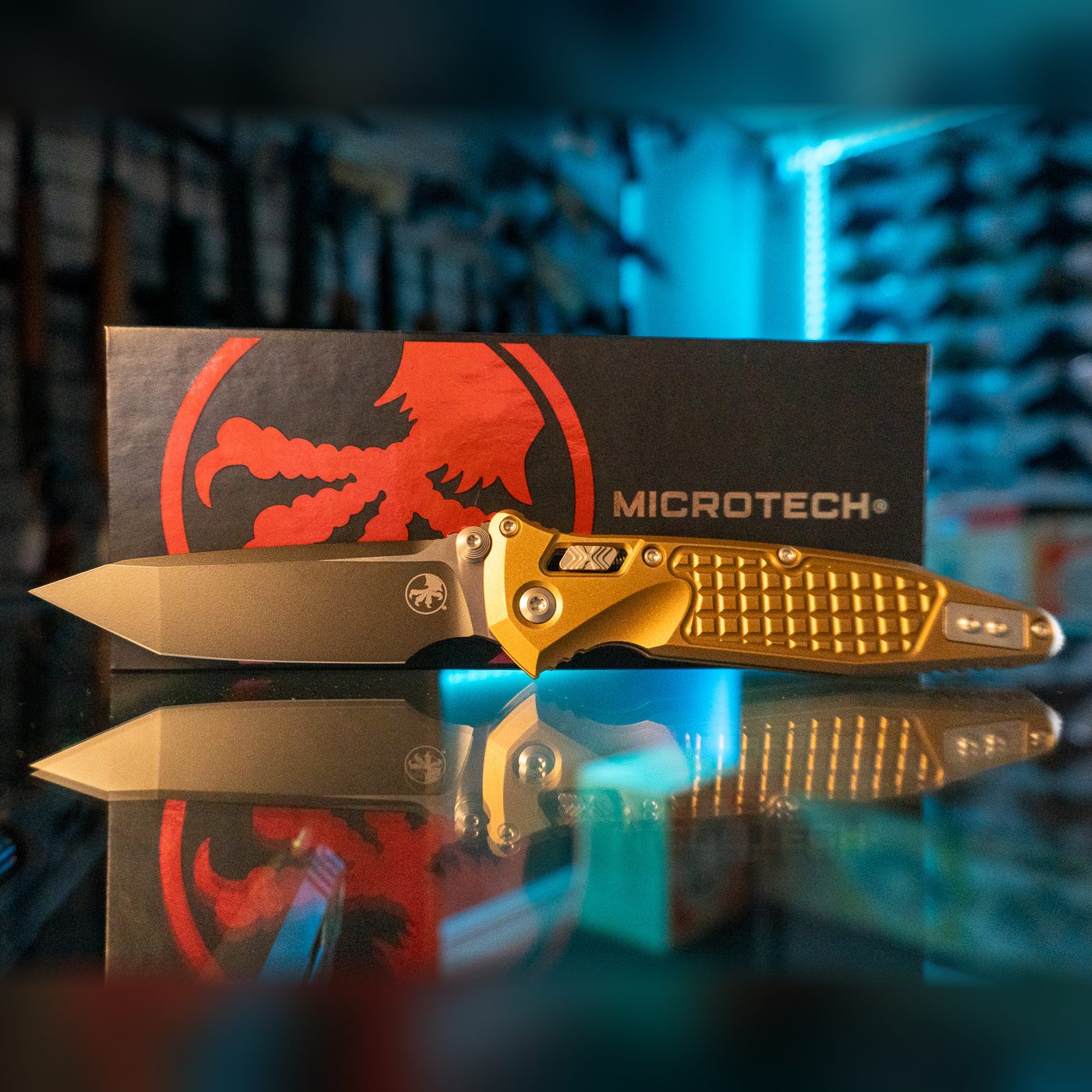 Microtech Socom RAM-LOK T/E folding knife with black tanto blade and tan frag-pattern aluminum handle on its Microtech box