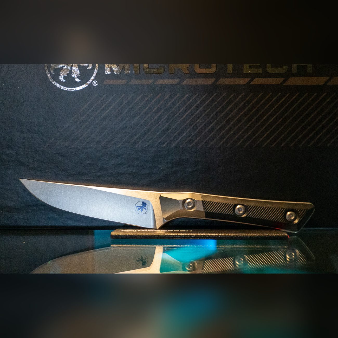 Microtech steak knife with stonewashed blade, black G-10 handle and titanium bolster in front of the black Microtech gift box