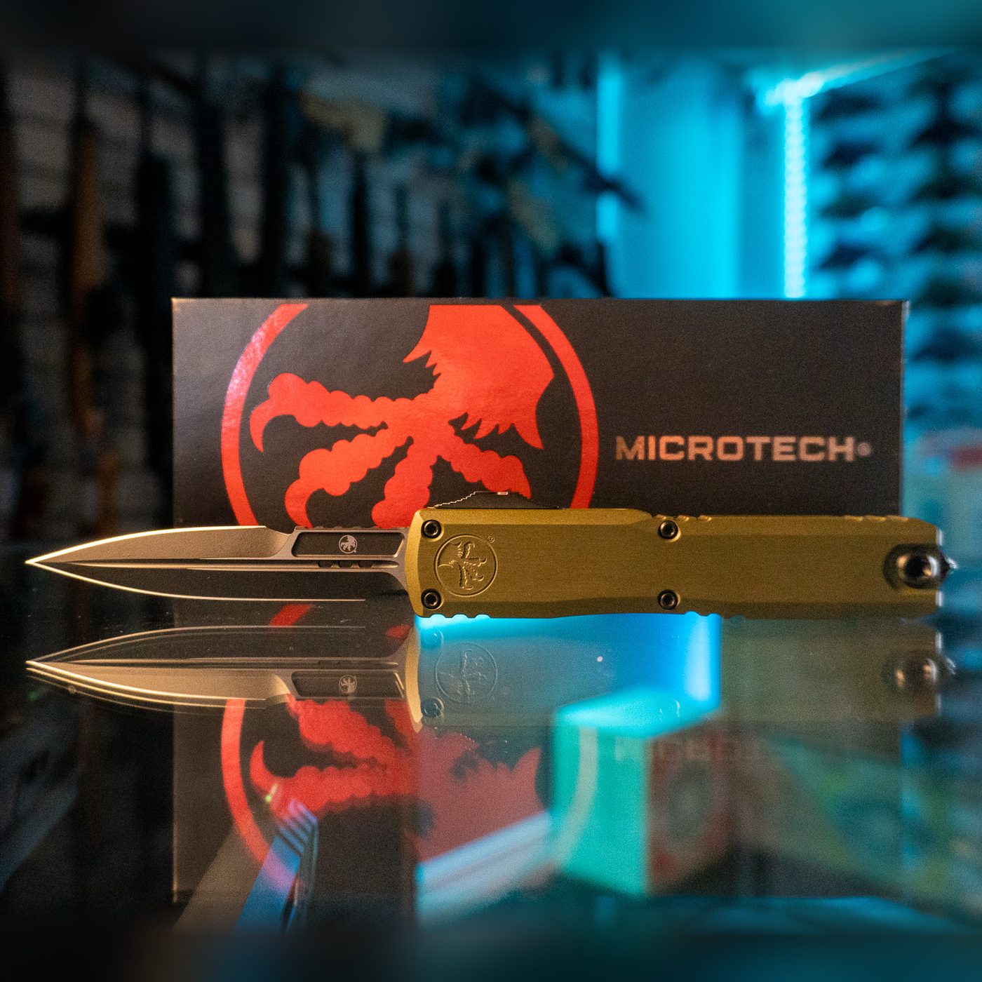 Microtech Ultratech Gen III ZBP OTF knife with black bayonet blade deployed and OD green aluminum handle, in front of its Microtech box