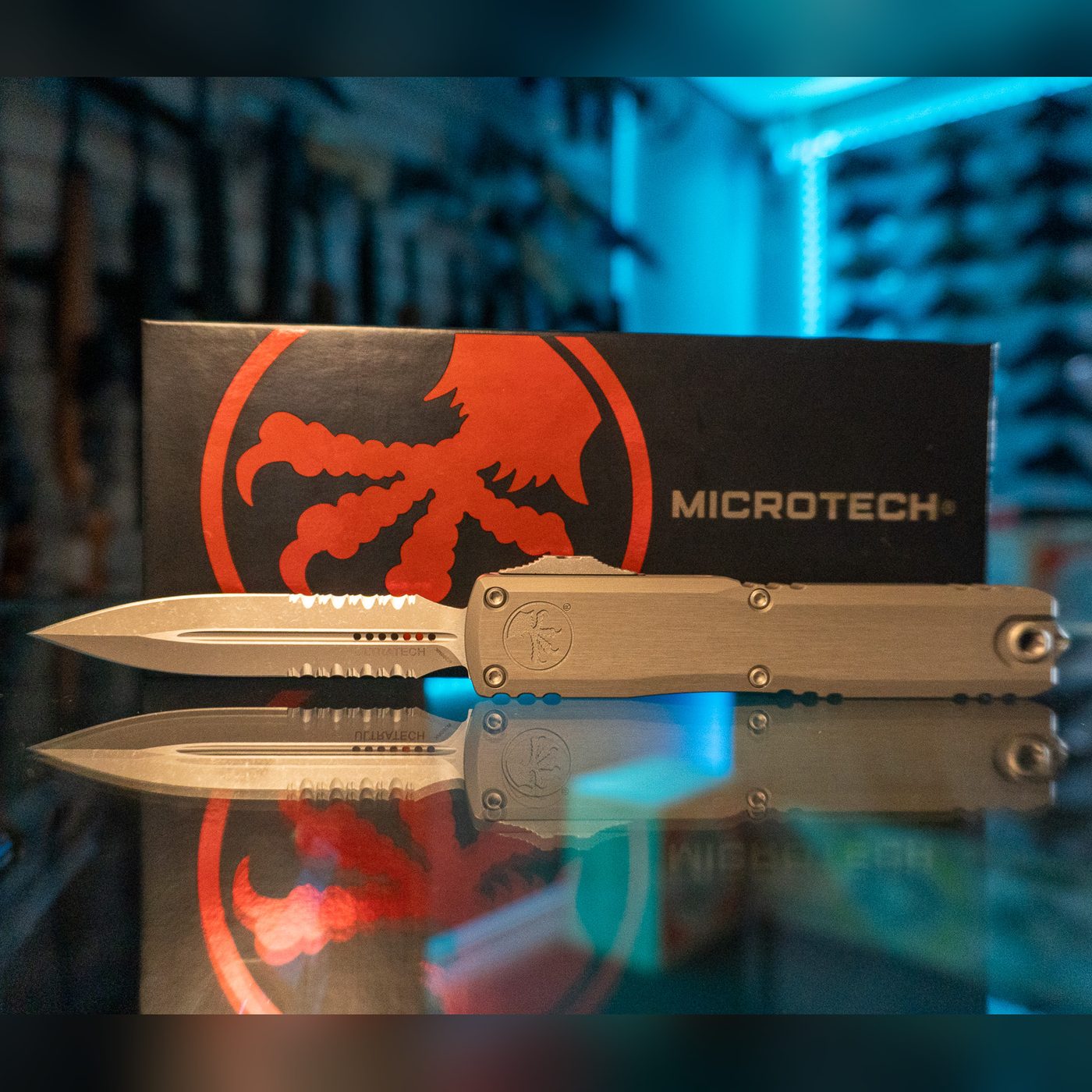 Microtech Ultratech Gen III ZBP OTF knife with apocalyptic double-edge partially serrated dagger blade deployed and natural clear aluminum handle, in front of its Microtech box