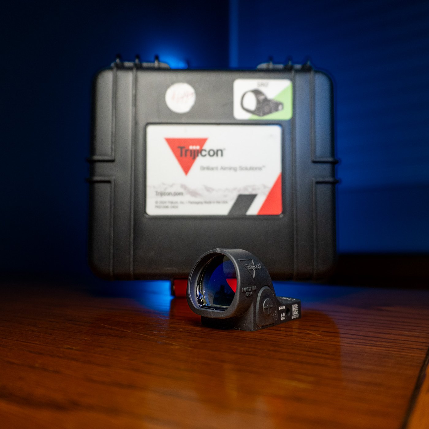 Trijicon SRO reflex pistol sight with 2.5 MOA green dot in matte black, hard case behind it on a wood table