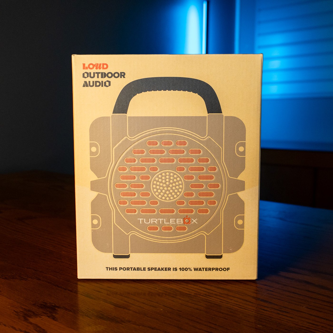 Turtlebox Cub portable Bluetooth speaker in tan, in its retail box on a wooden table
