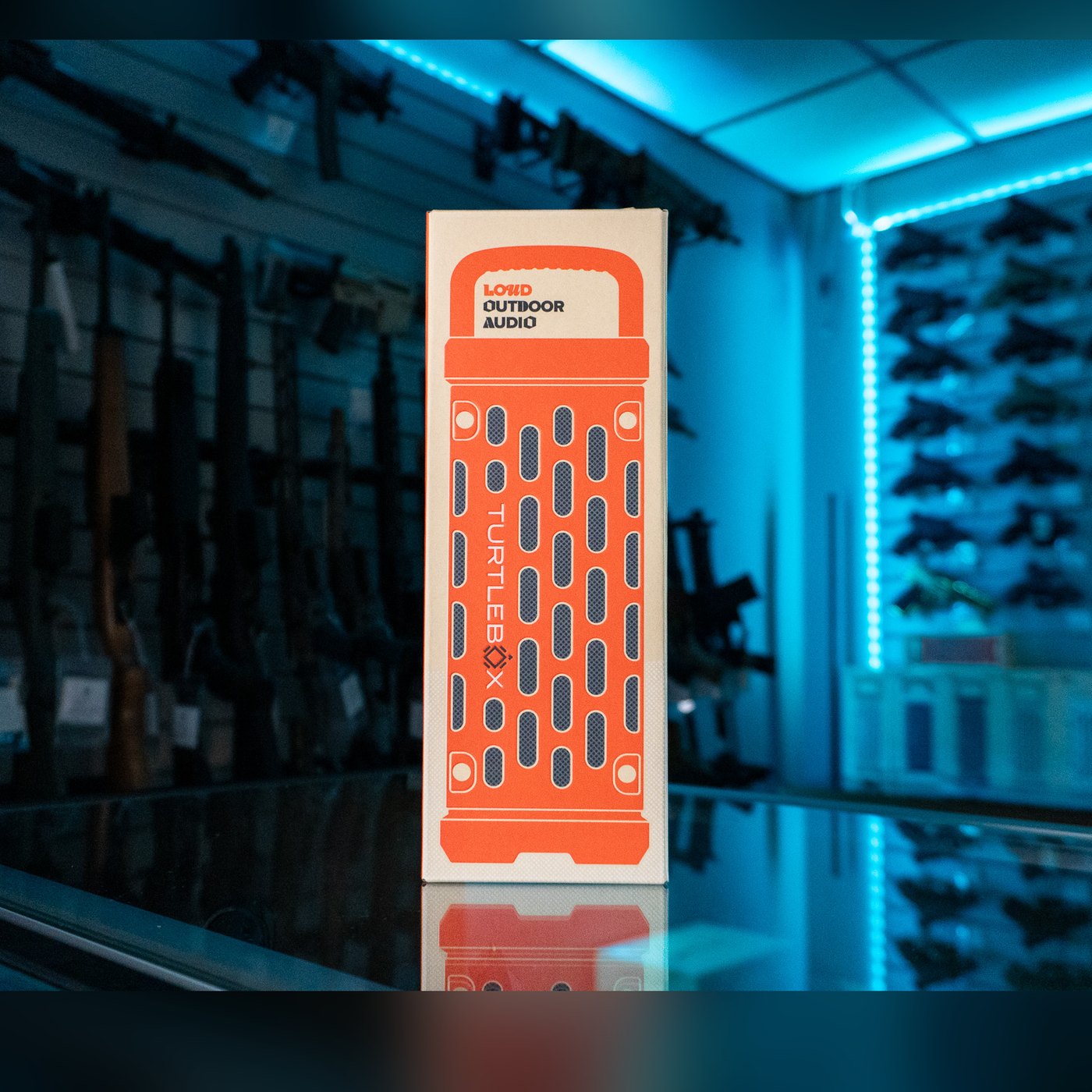 Turtlebox Ranger speaker retail box in orange and cream, printed with a speaker grille design and "Loud Outdoor Audio", standing on a glass display counter